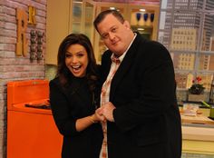 a man and woman standing next to each other in front of a brick wall with an orange refrigerator