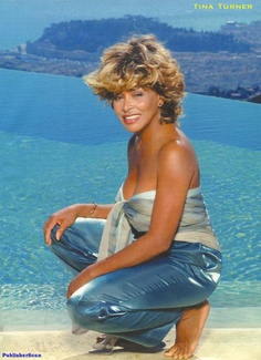 a woman sitting on top of a sandy beach next to the ocean with her legs crossed