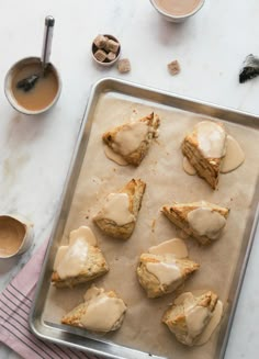 a pan filled with scones covered in icing next to cups and spoons