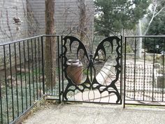 an iron gate with a potted plant in the middle and a butterfly design on it