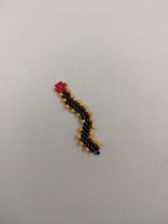 a single beaded flower on a white surface with yellow and black beads around it