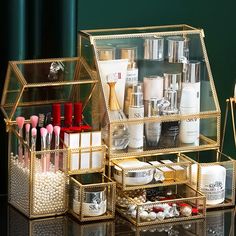 an assortment of beauty products displayed in gold containers on a black counter top with green wall behind it