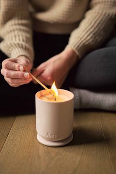 a person lighting a candle with a stick in their hand while sitting on the floor