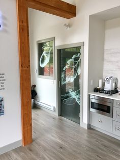 a kitchen with white walls and wood flooring next to an open door that leads to another room