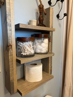 a wooden shelf with toilet paper and other items on it next to a white toilet