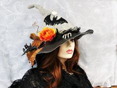 a woman wearing a black hat with orange flowers on the brim and leaves attached to it