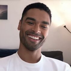 a man smiling and wearing a white t - shirt