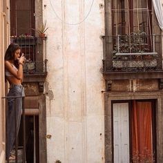 a woman is standing on the balcony talking on her cell phone while looking out at the street