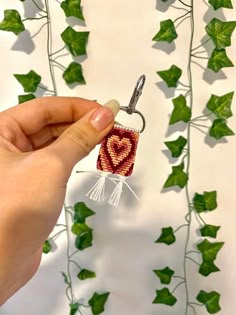 a hand holding a keychain with a heart on it in front of ivy leaves