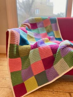 a multicolored blanket sitting on top of a pink chair next to a window