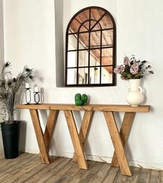 a wooden table with two vases on it next to a mirror and potted plant