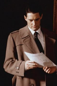 a man in a suit and tie is reading a piece of paper while looking at something