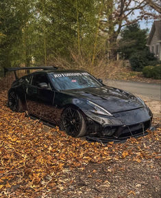 a black sports car parked on top of leaves next to a road with trees in the background