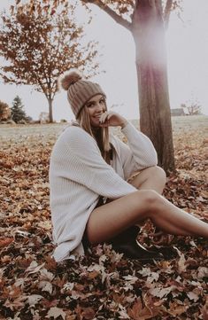 a woman sitting on the ground with her legs crossed and wearing a knitted hat