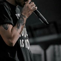 a man holding a microphone in his right hand and wearing a black t - shirt