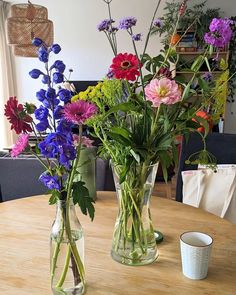 two vases filled with colorful flowers sitting on top of a wooden table next to a cup