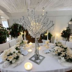 a dining room table is set with white flowers and candles for an elegant centerpiece