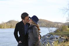 a man and woman standing next to each other by the water kissing on their foreheads