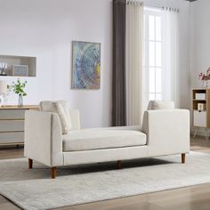 a living room with a white couch and rug in front of a large window that has curtains on the windowsill