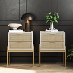 two white and gold nightstands with plants on them in front of a black wall