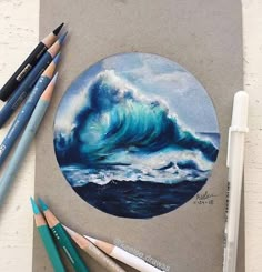 some colored pencils are laying next to a drawing of a wave in the ocean