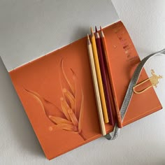 an orange notebook with pencils on top of it