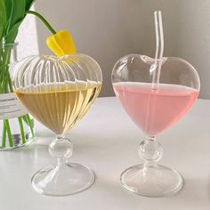 two heart shaped vases filled with liquid on top of a white table next to flowers