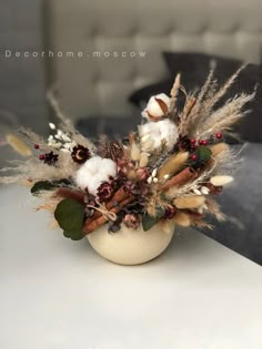 a white vase filled with lots of dried flowers and feathers on top of a table