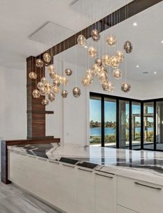 a modern kitchen with marble counter tops and hanging lights over the island in front of large windows