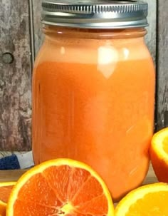 an orange juice in a glass jar next to sliced oranges on a wooden table