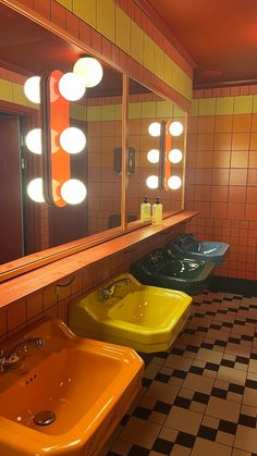 three sinks in a bathroom with mirrors and lights on the wall above them are yellow, green, and blue