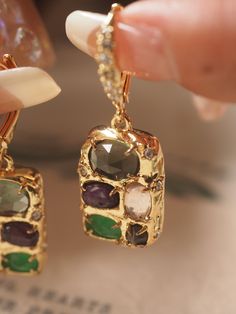 Elevate your style with these Ren Multi-Gemstone Drop Earrings, a true statement of elegance and sophistication. Featuring a vibrant array of gemstones in rich hues of green, purple, and clear, each piece is meticulously set in a lustrous gold-tone frame that captures light from every angle. The earrings are adorned with sparkling cubic zirconia accents along the lever-back hooks, adding an extra touch of glamour. Crafted for those who appreciate unique and artistic designs, these drop earrings combine classic luxury with a contemporary twist. Perfect for special occasions or adding a touch of elegance to your everyday look, these earrings are designed to stand out and make a lasting impression. Details: Material: Gold pleated metal Gemstones: Multi-colored stones (green, purple, clear) wi Gold Plated Drop Earrings With Gemstone Accents, Fine Jewelry Earrings With Gemstone Accents For Party, Fine Jewelry Party Earrings With Gemstone Accents, Elegant Green Multi-stone Gemstones, Party Green Gold-plated Earrings, Luxury Green Multi-stone Earrings, Elegant Emerald Earrings With Gemstone Accents, Elegant Multi-stone Emerald Jewelry, Elegant Multi-stone May Birthstone Jewelry