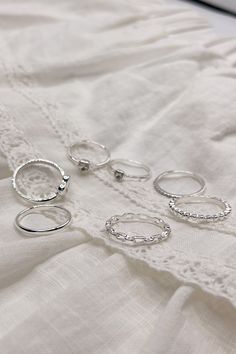 The Veronica Heart Ring Set is a charming collection of seven rings, available in silver or gold and sized at 7. This versatile set includes a variety of designs to suit any style: one ring features an open heart, two rings showcase rhinestone hearts, one plain band offers simplicity, one band is adorned with sparkling rhinestones, one chainlink band adds a unique touch, and one notched band completes the set. Perfect for mixing and matching, the Veronica Heart Ring Set is a delightful way to ac Trendy Silver Rings For Wedding, Trendy Silver Heart Ring For Anniversary, Dainty Silver Midi Rings, Dainty Silver Metal Midi Rings, Silver Heart Open Ring For Everyday, Everyday Silver Heart Open Ring, Silver Open Heart Ring For Everyday, Trendy Silver Heart Promise Ring, Silver Trendy Heart Promise Ring