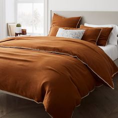 the bed is made with brown linens and white pillows, along with an orange comforter