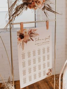 a wedding seating chart hanging on a metal stand with dried flowers and foliage in the background