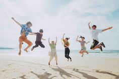 four people jumping in the air on a beach with their arms up and legs spread out