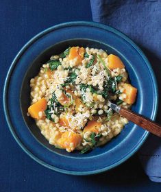 a bowl filled with rice and vegetables on top of a blue cloth next to a wooden spoon