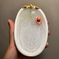 a hand holding a white bowl with a toy pig in it's mouth and water on the inside