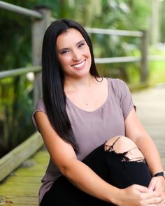 a smiling woman sitting on a wooden walkway