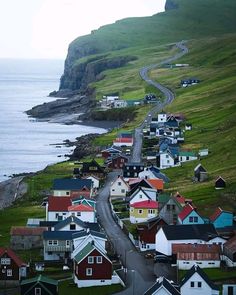 an aerial view of a small town by the ocean with mountains in the background and green grass on both sides