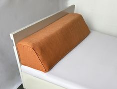 an orange pillow sitting on top of a white bed