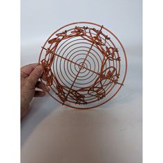 a hand holding a wire sculpture on top of a white table with an orange spiral design