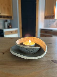 a lit candle sitting in a bowl on top of a wooden table