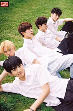 group of young men sitting on the grass in front of each other with their hands behind their backs