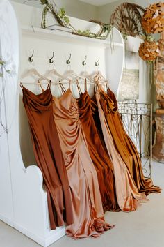 there are many different colored dresses hanging on the rack in front of a white bench