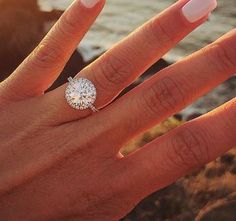 a woman's hand with a diamond ring on it and the ocean in the background