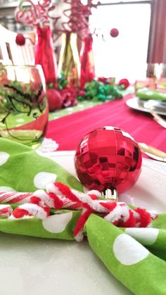 the table is set for christmas dinner with red and green napkins, silverware, and ornaments