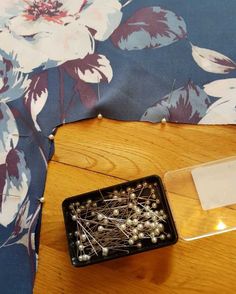 a wooden table topped with a black container filled with pins