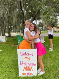 two girls hugging each other in front of a sign