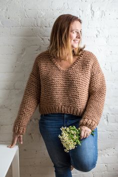 a woman is standing in front of a white brick wall holding a bouquet of flowers